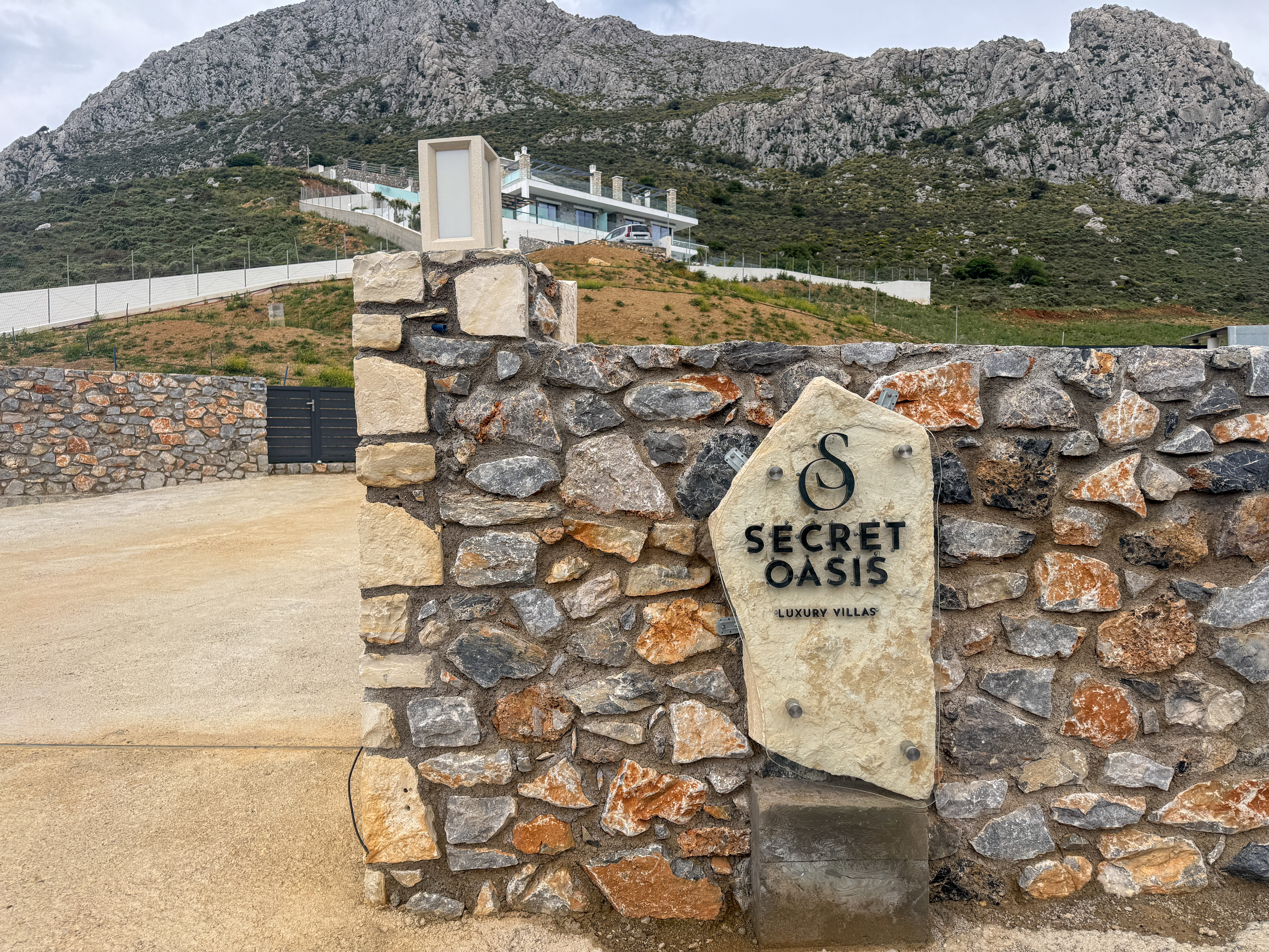 Secret Oasis stone entrance with logo and the villa on the mountainside in the background, Plakias South Crete