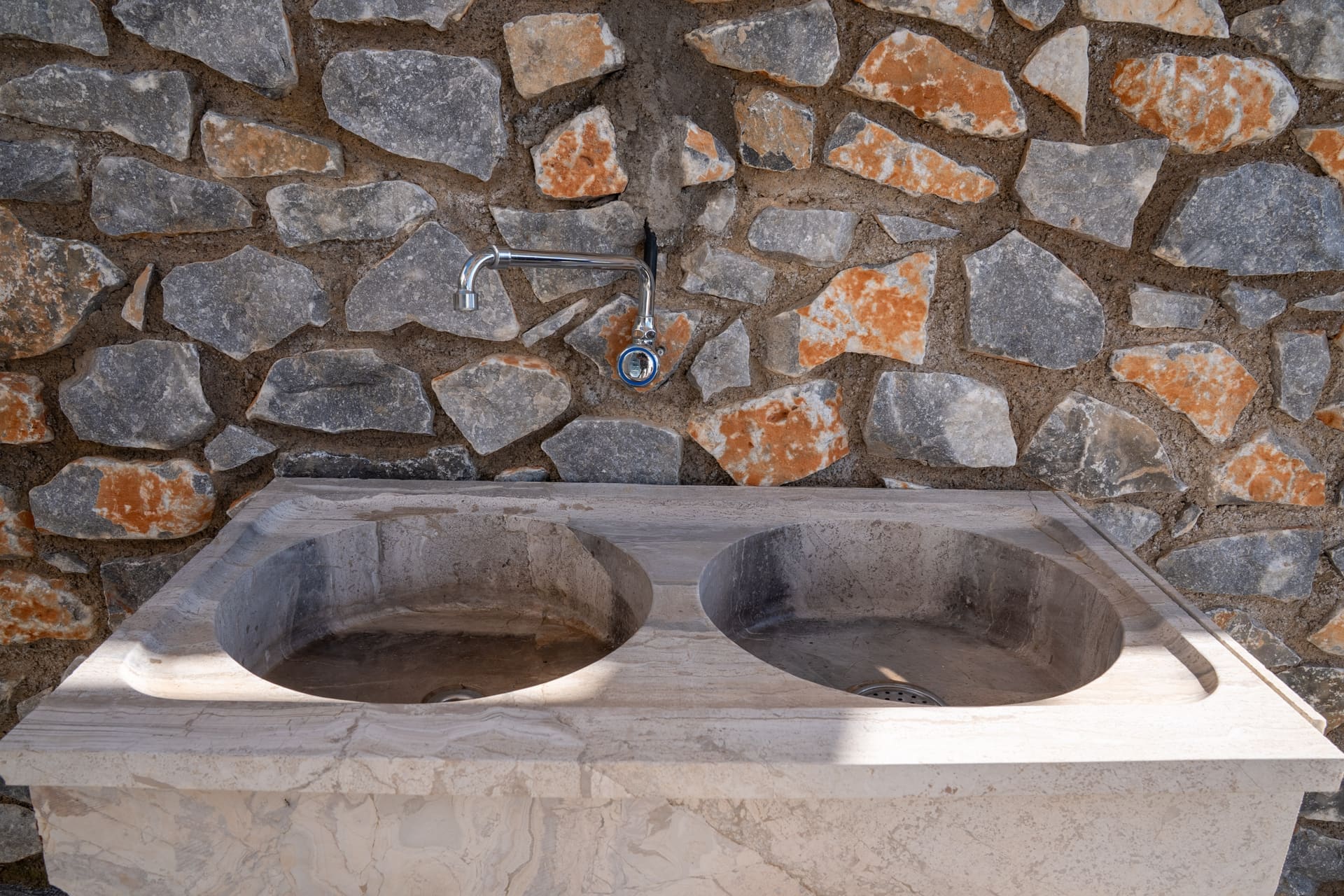 Outdoor kitchen with double stone sink against a natural stone wall at the BBQ Endless View