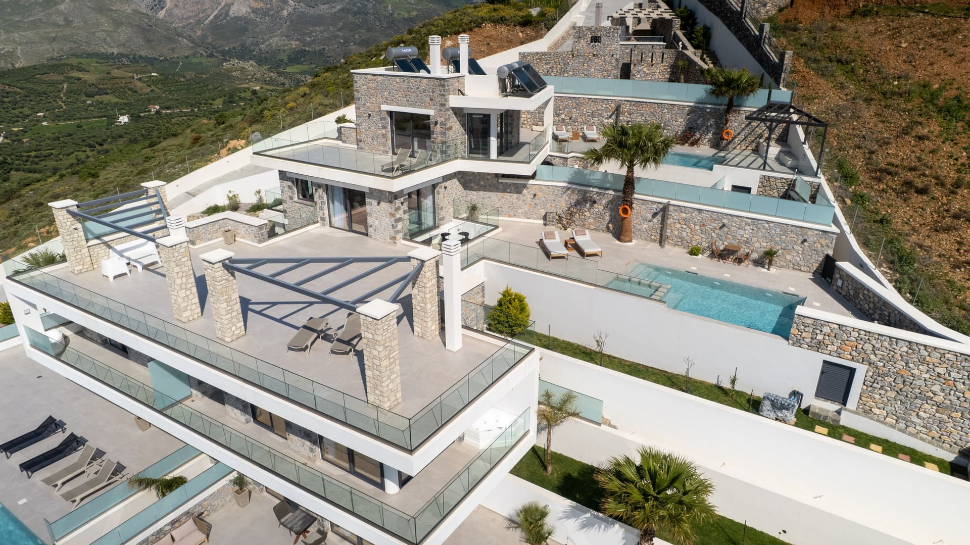 Villa in Plakias with sea view — drone shot of Secret Oasis hill compound with private pools and Plakias Bay in the background